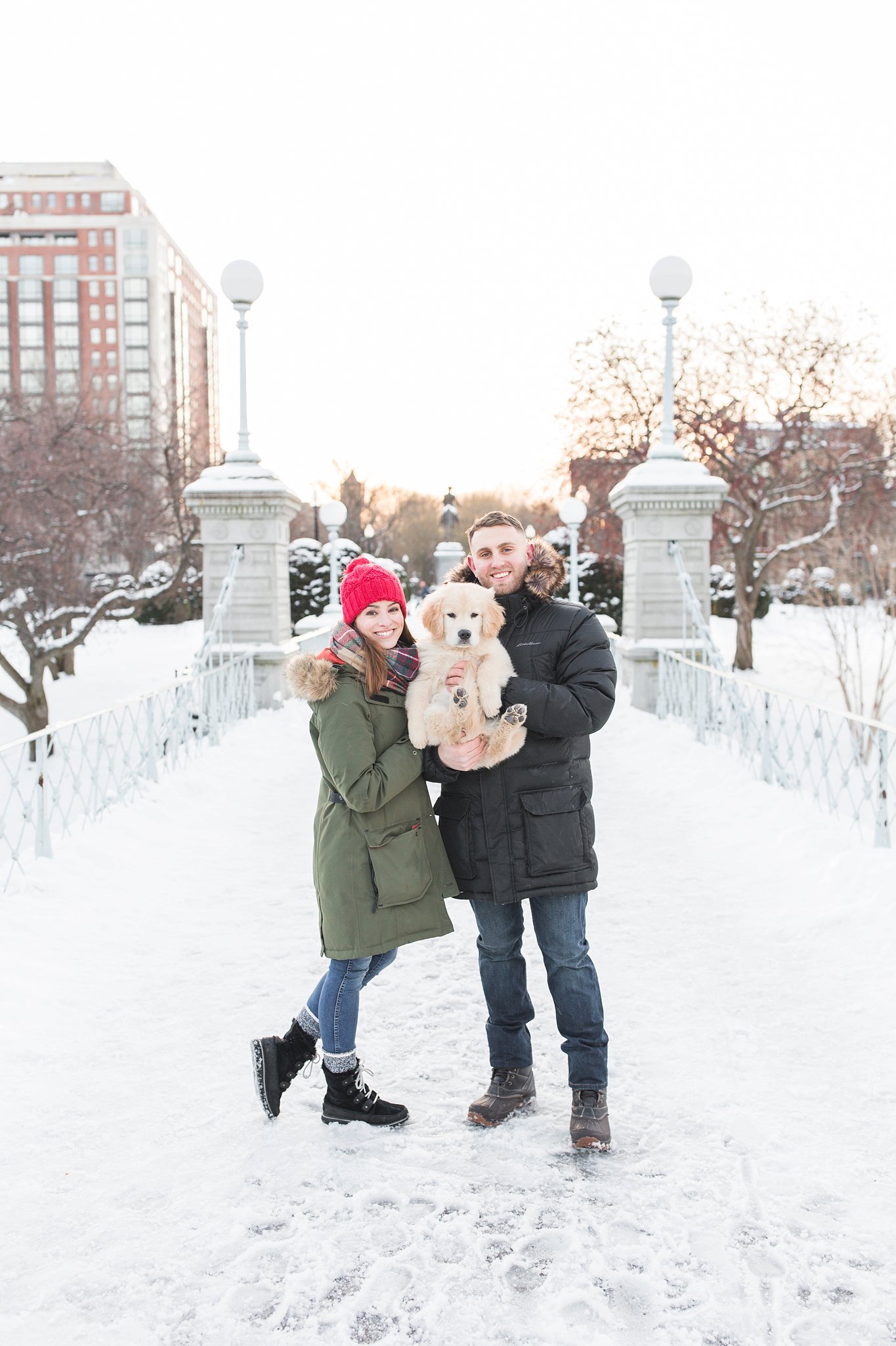 couple holding a golden retriever puppy on the snowy bridge in the Public Garden in Boston