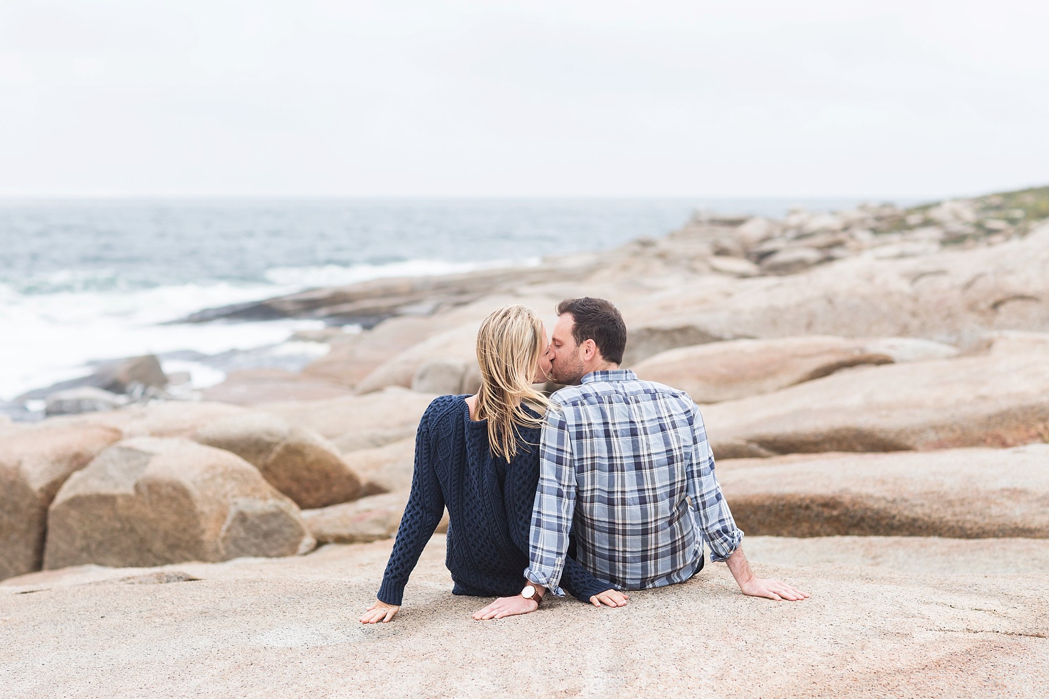 a man and woman sitting on the rocks kissing at halibut point state park
