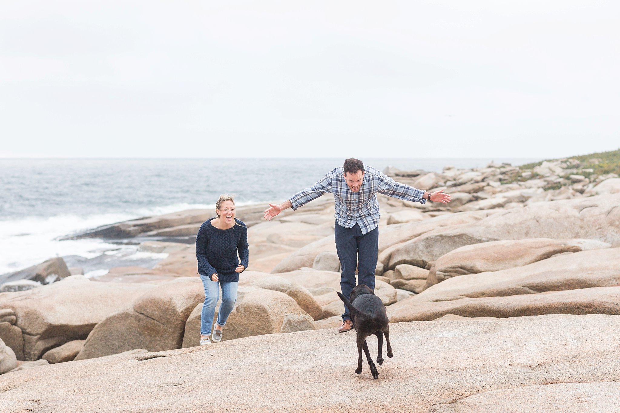 a man and woman playing with their dog on the rocks at halibut point state park