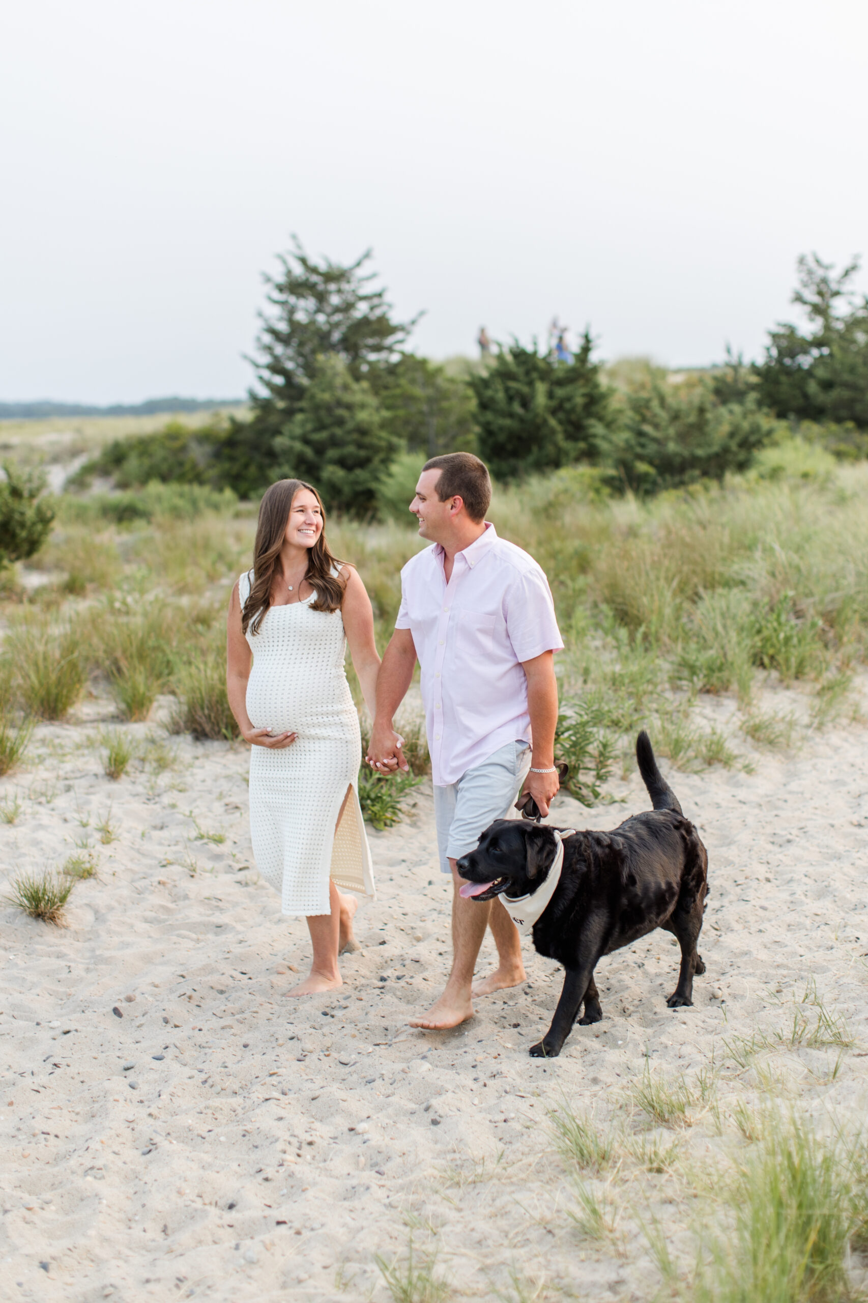 Parents walking on the beach with their dog, with woman holding her baby bump