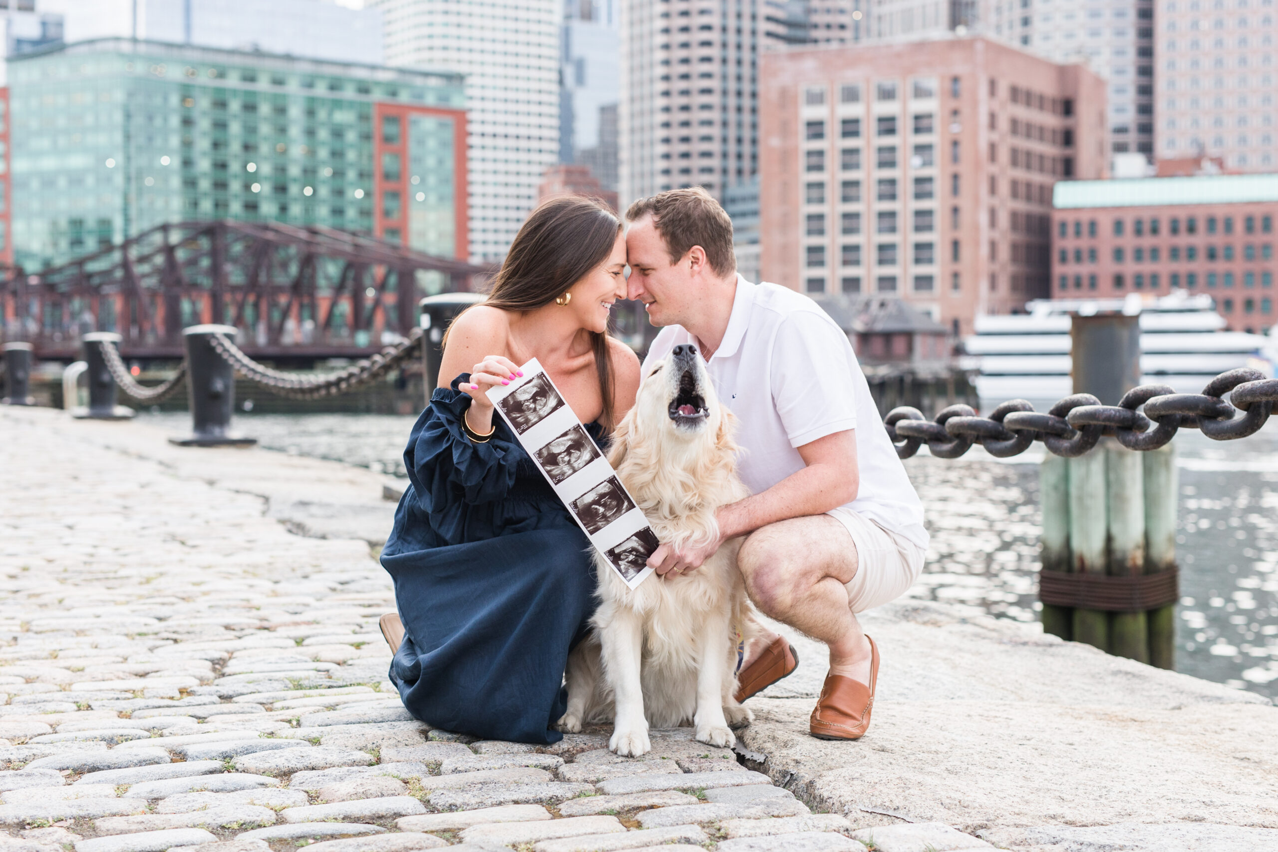 Couple holding up pregnancy announcement with their dog howling in between them
