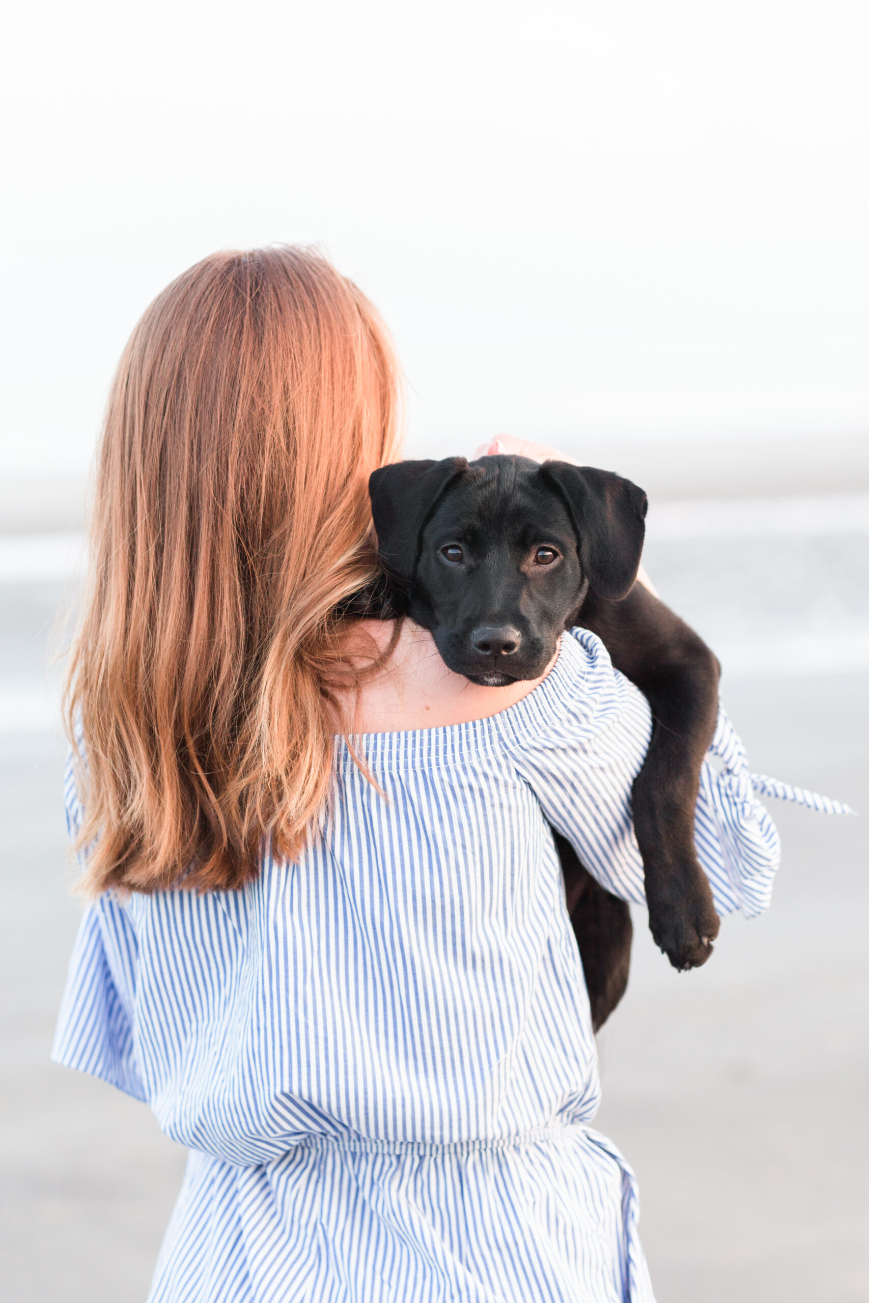 Girl holding her puppy with its head on her shoulder