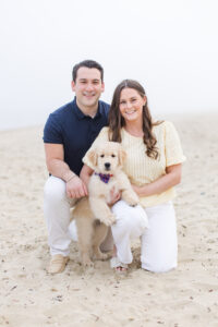 Couple on a beach with their golden retriever puppy wearing a bowtie during a Puppy Photoshoot.
