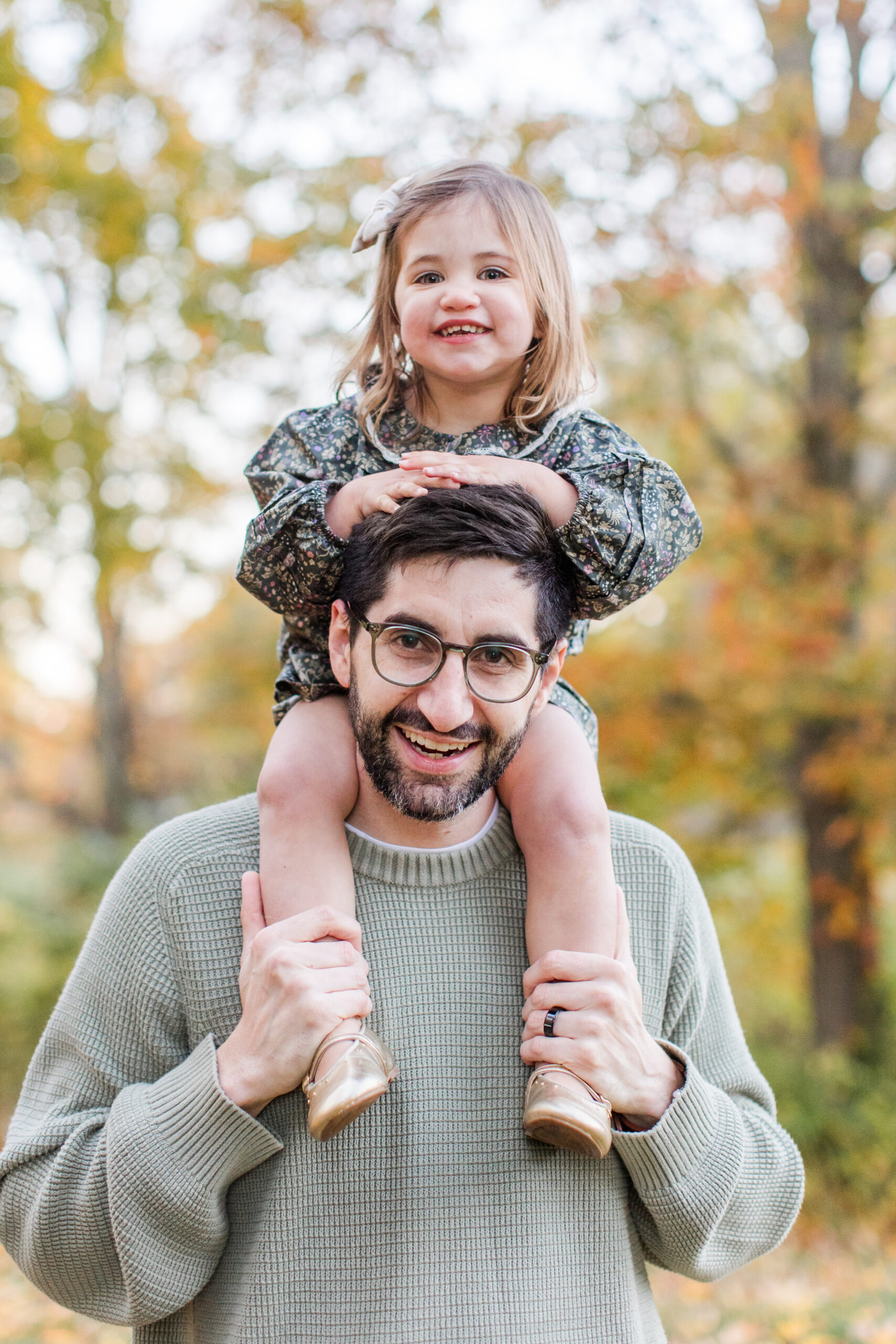 A little girl sitting on her dad's shoulders during fall family photoshoot
