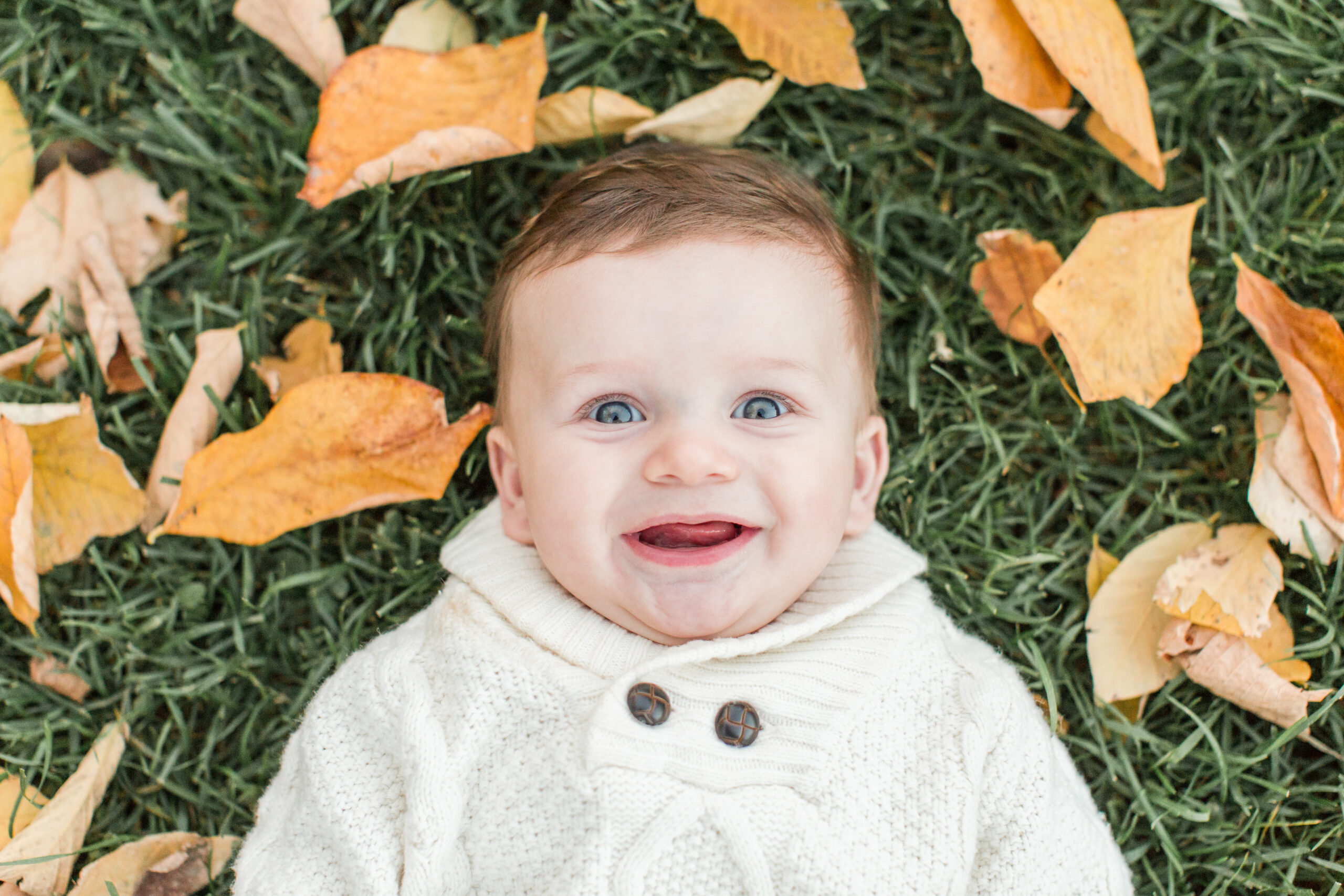 A baby laying on the ground with leaves around him
