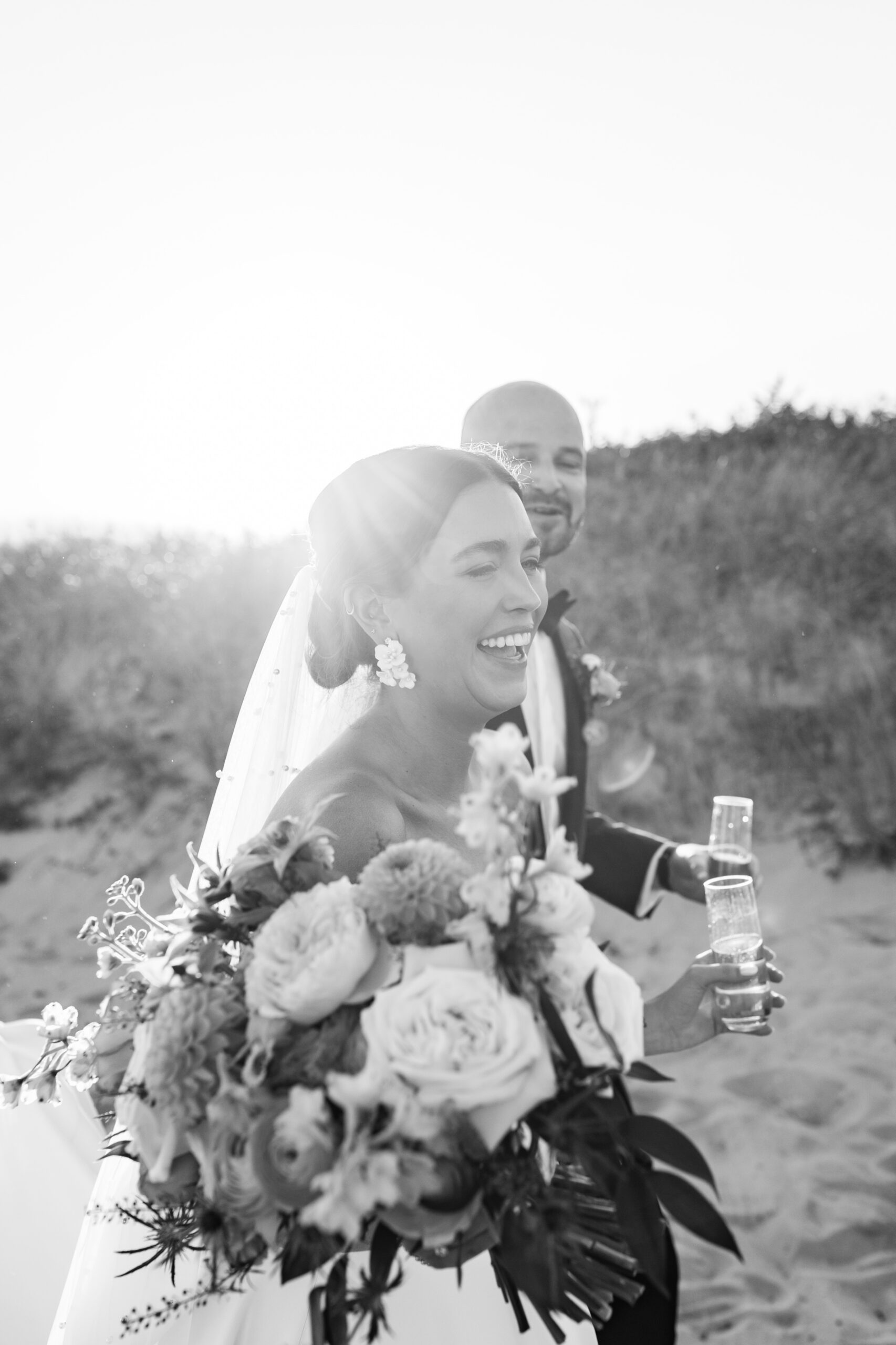 A black and white photo of a bride and groom walking on the beach