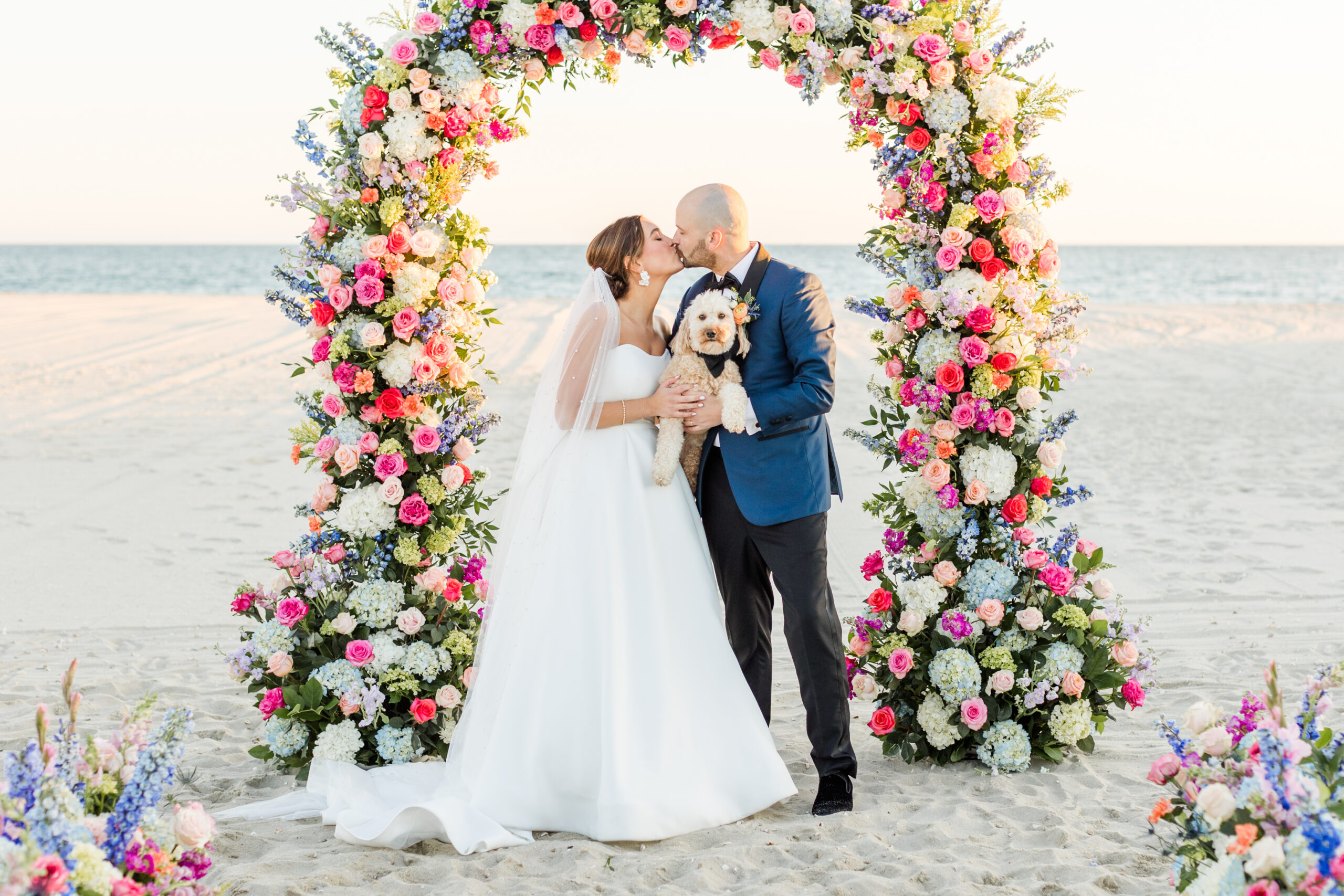 A couple kissing at their Wychmere beach club wedding holding their dog
