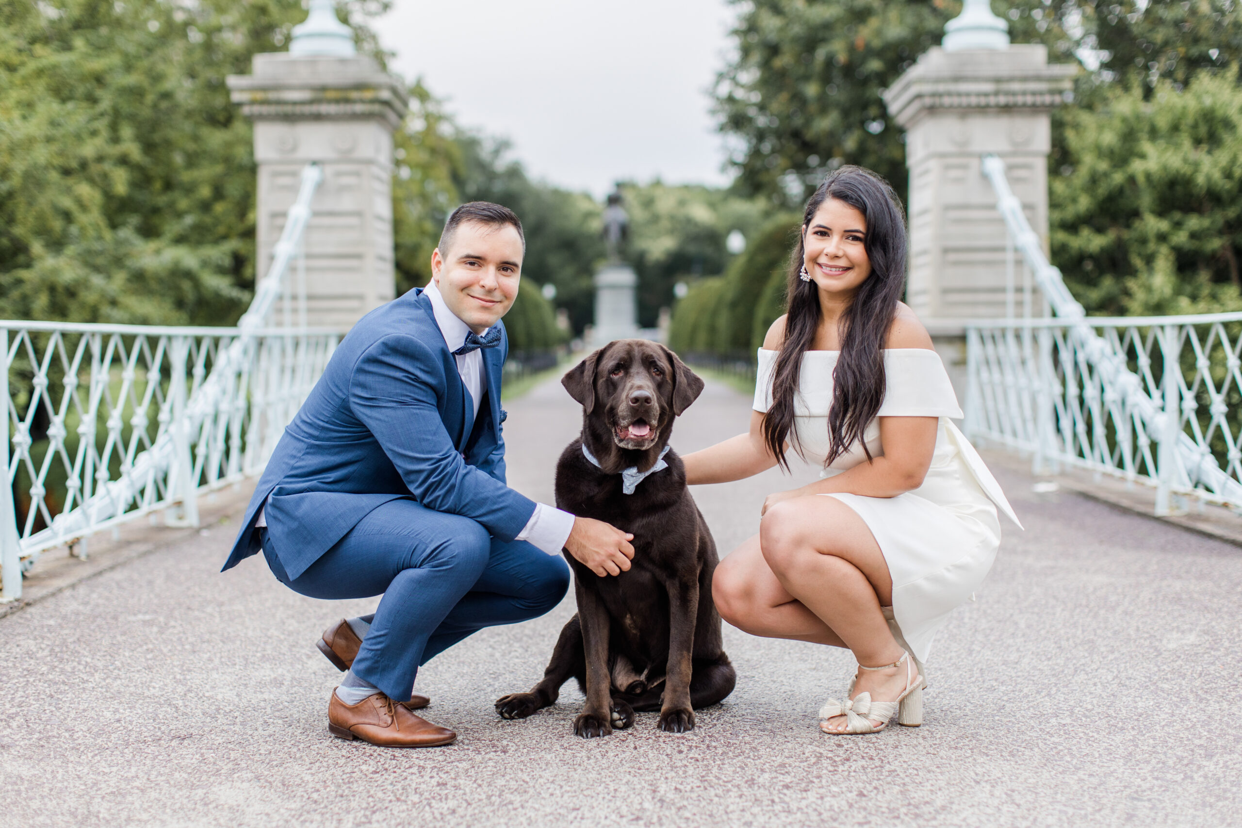 A couple posing for Boston engagement photos with their dog on the Public Garden bridge