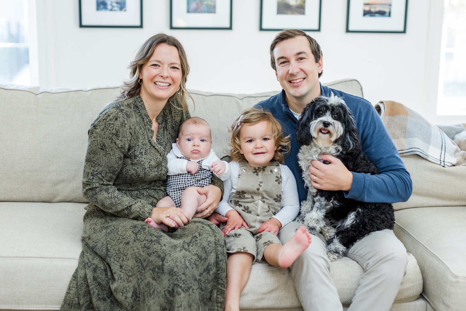 Man, woman, toddler and baby with dog sitting on couch
