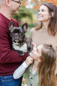 Man and woman smile at each other and little girl looks at a dog in the man's arms