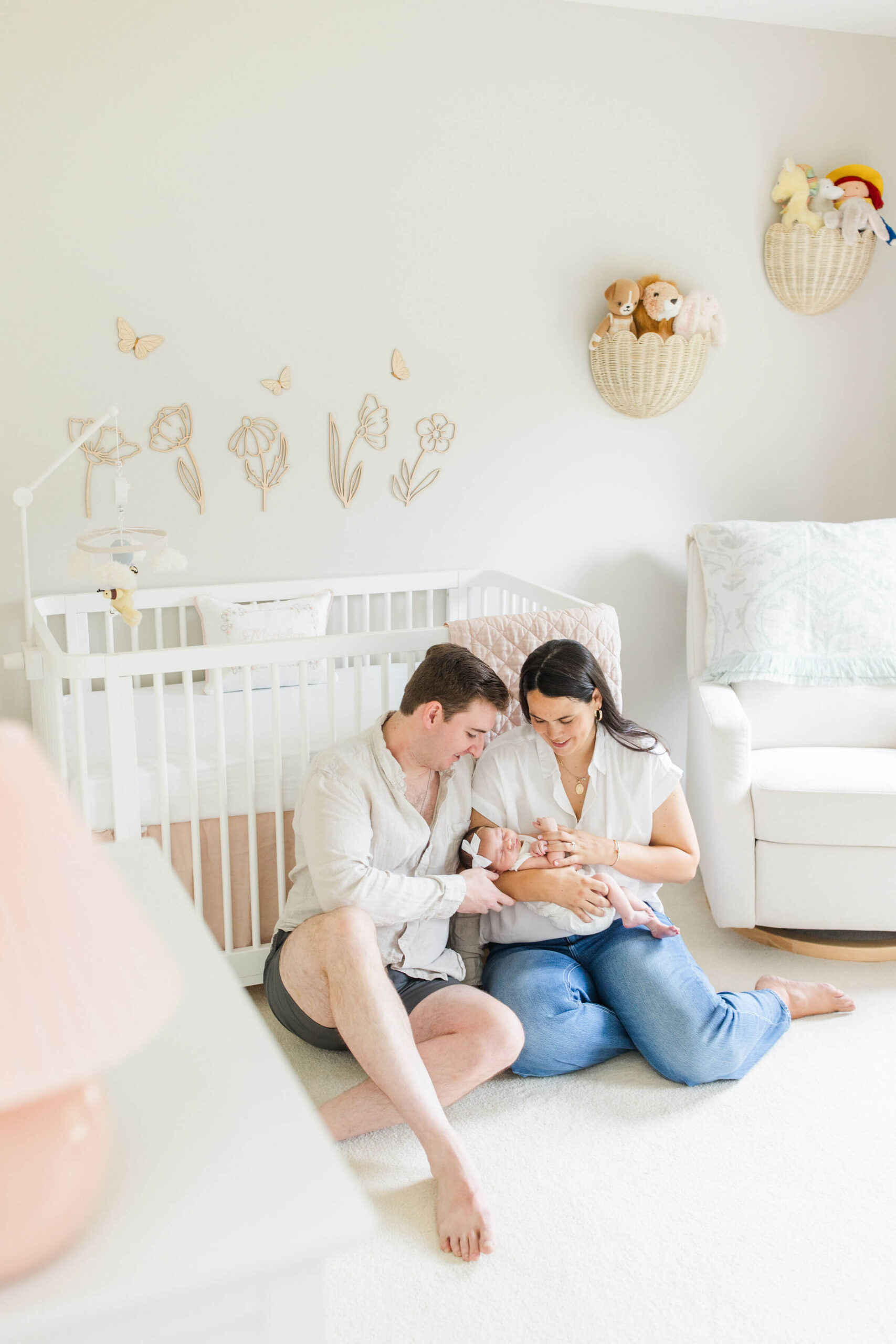 New parents sitting on the nursery floor holding their baby girl during a cozy in-home newborn session.