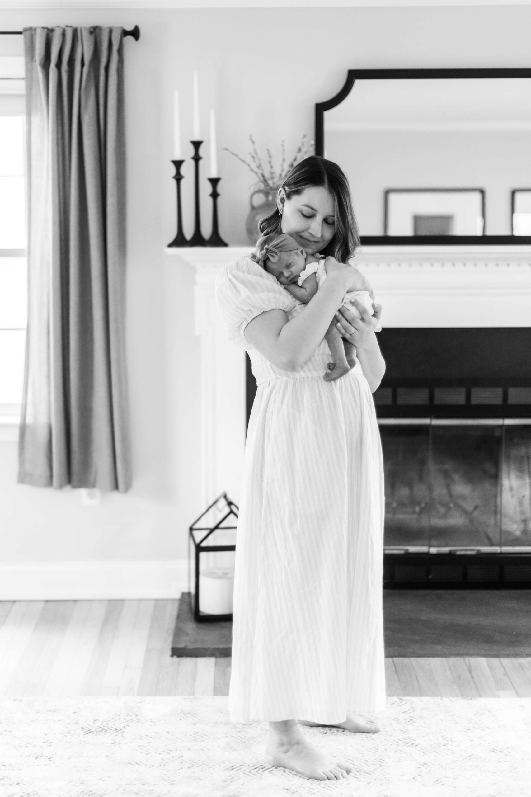 Mother holding her newborn baby against her chest in a black-and-white portrait inside their home.