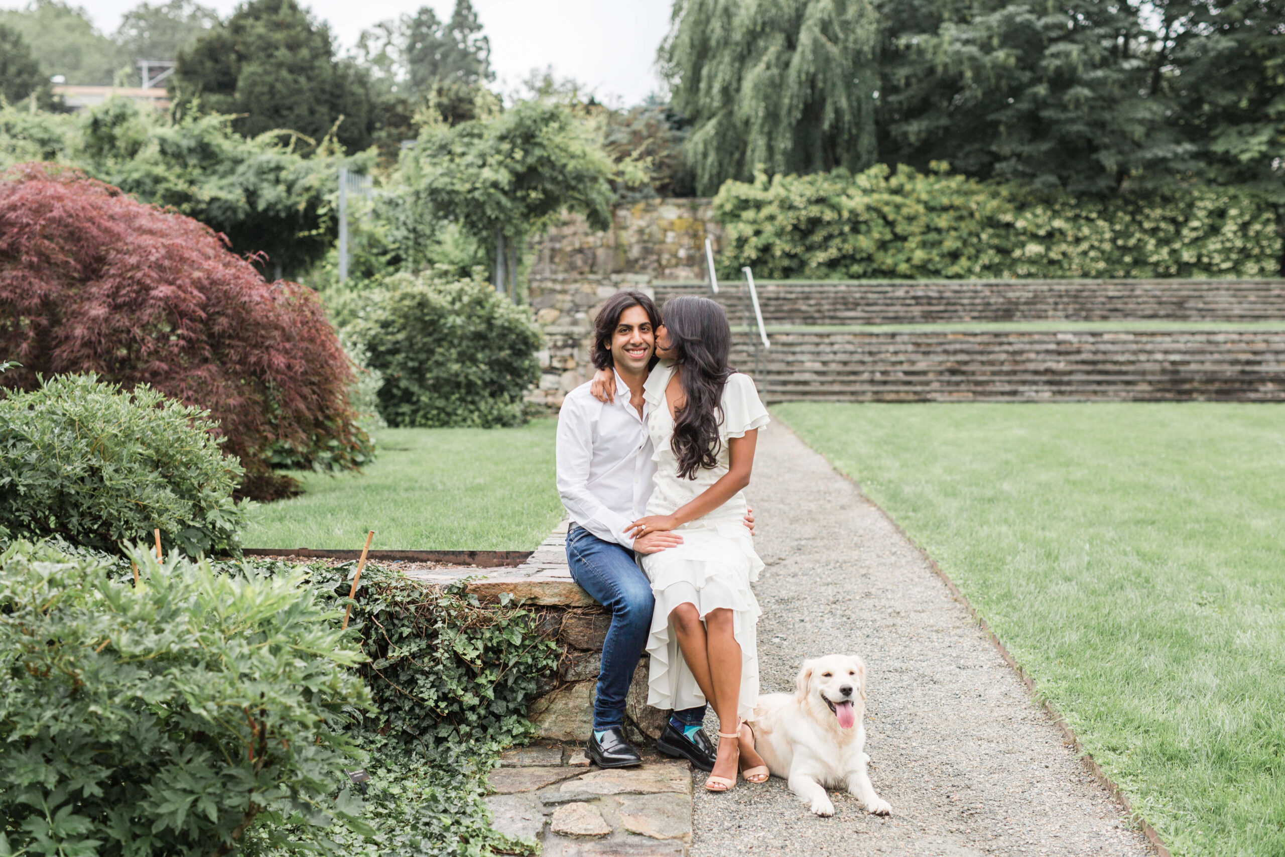 Couple sitting beside her their small dog in a landscaped garden.