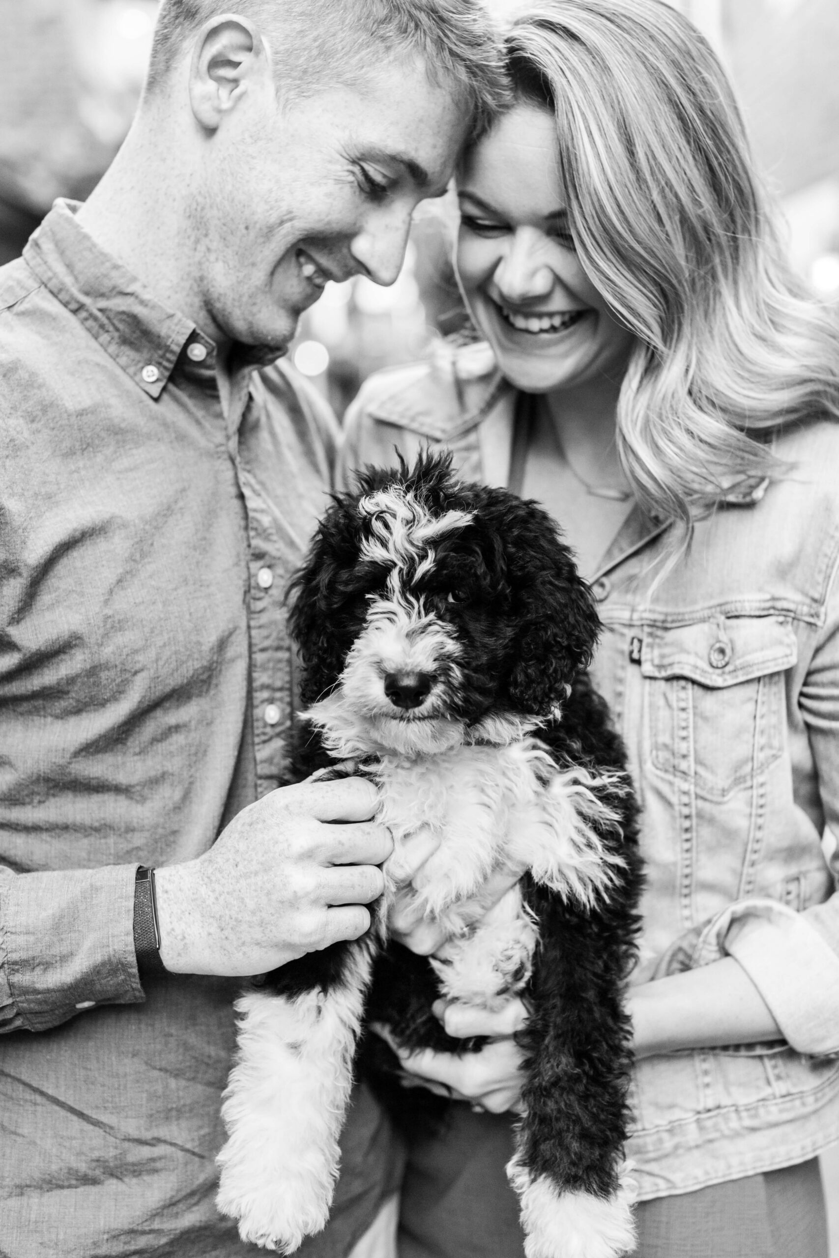 Couple holding their fluffy black-and-white puppy in a black-and-white portrait.