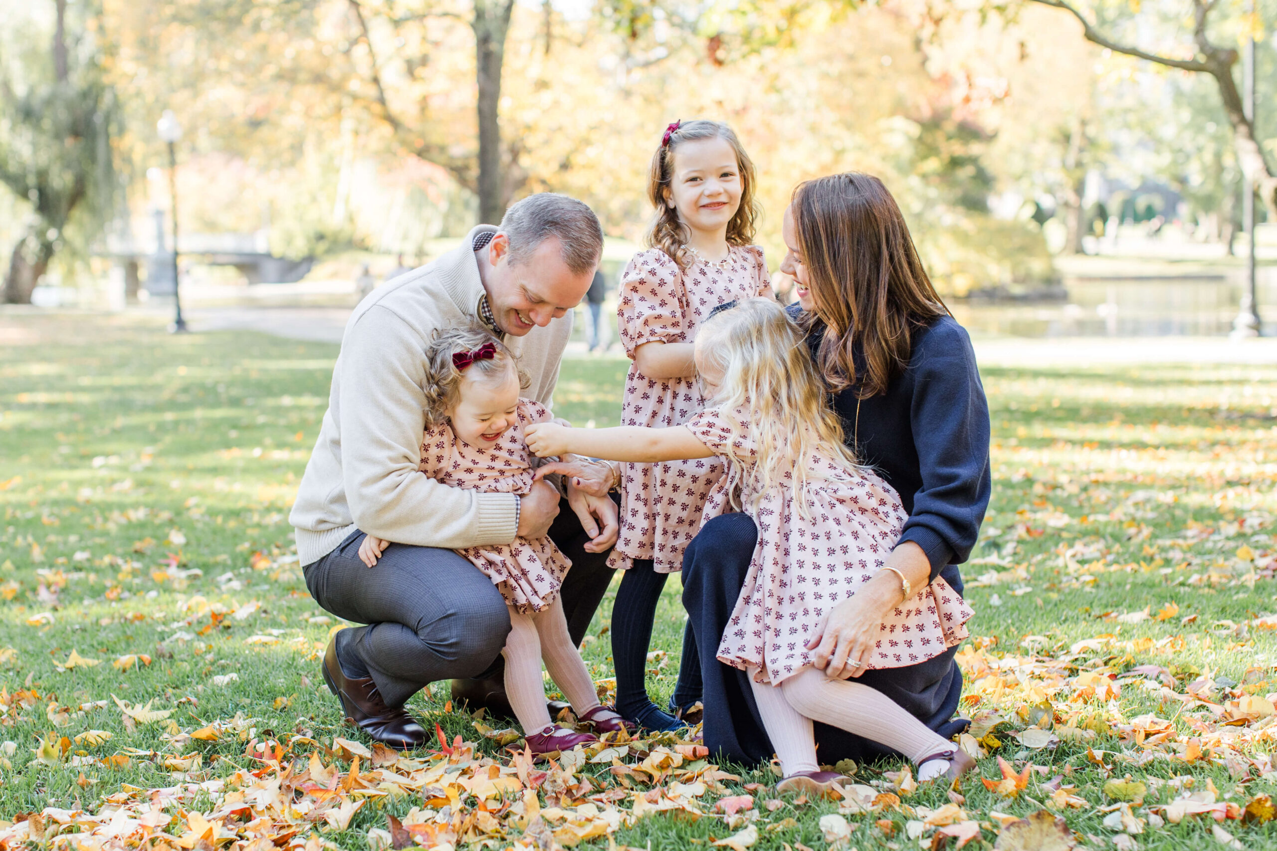 Family of five laughing together in a leaf-covered park during a fall family photo session.