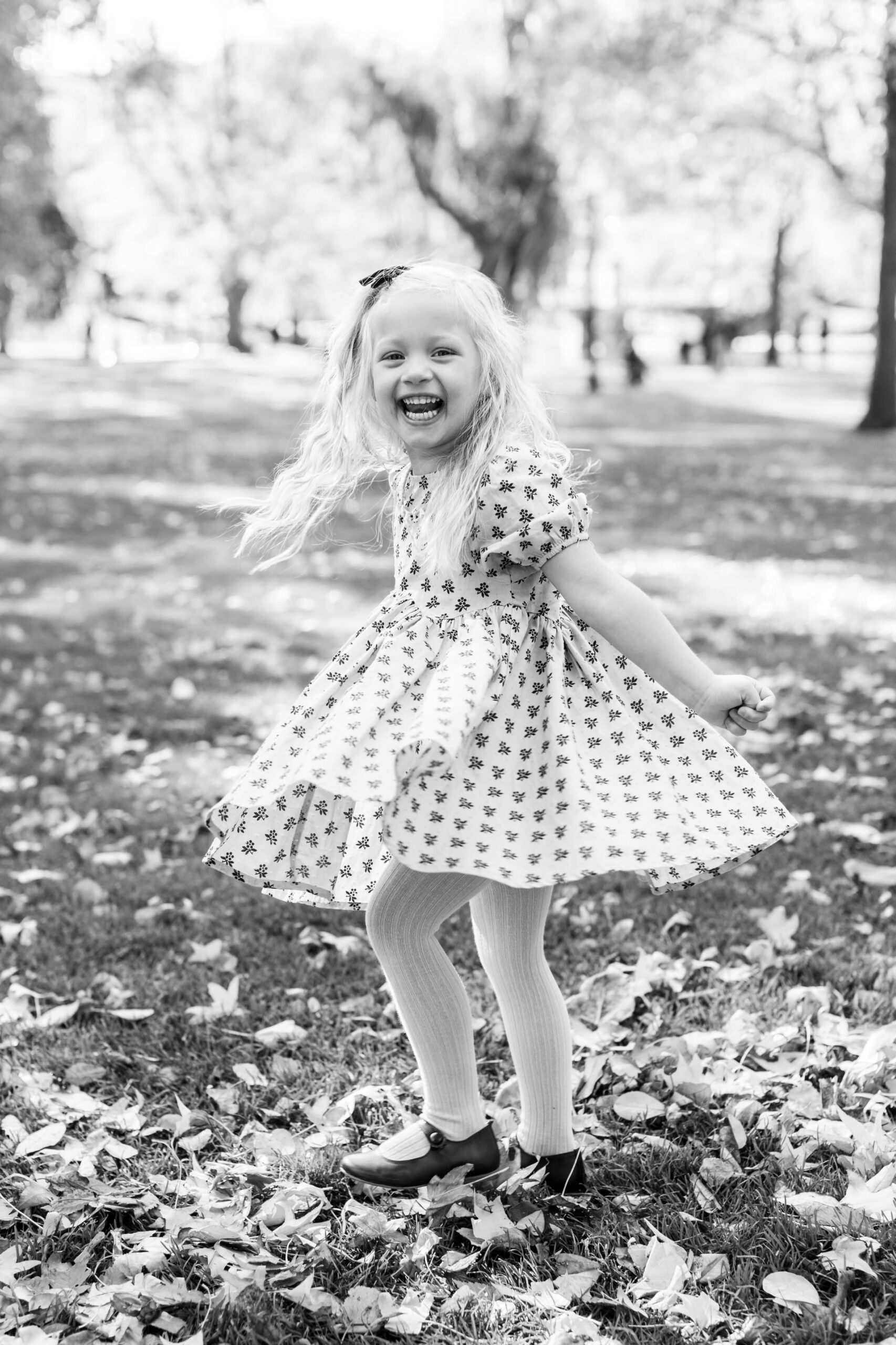 Black-and-white photo of a young girl twirling in her dress during a fall mini session at Boston Public Garden.