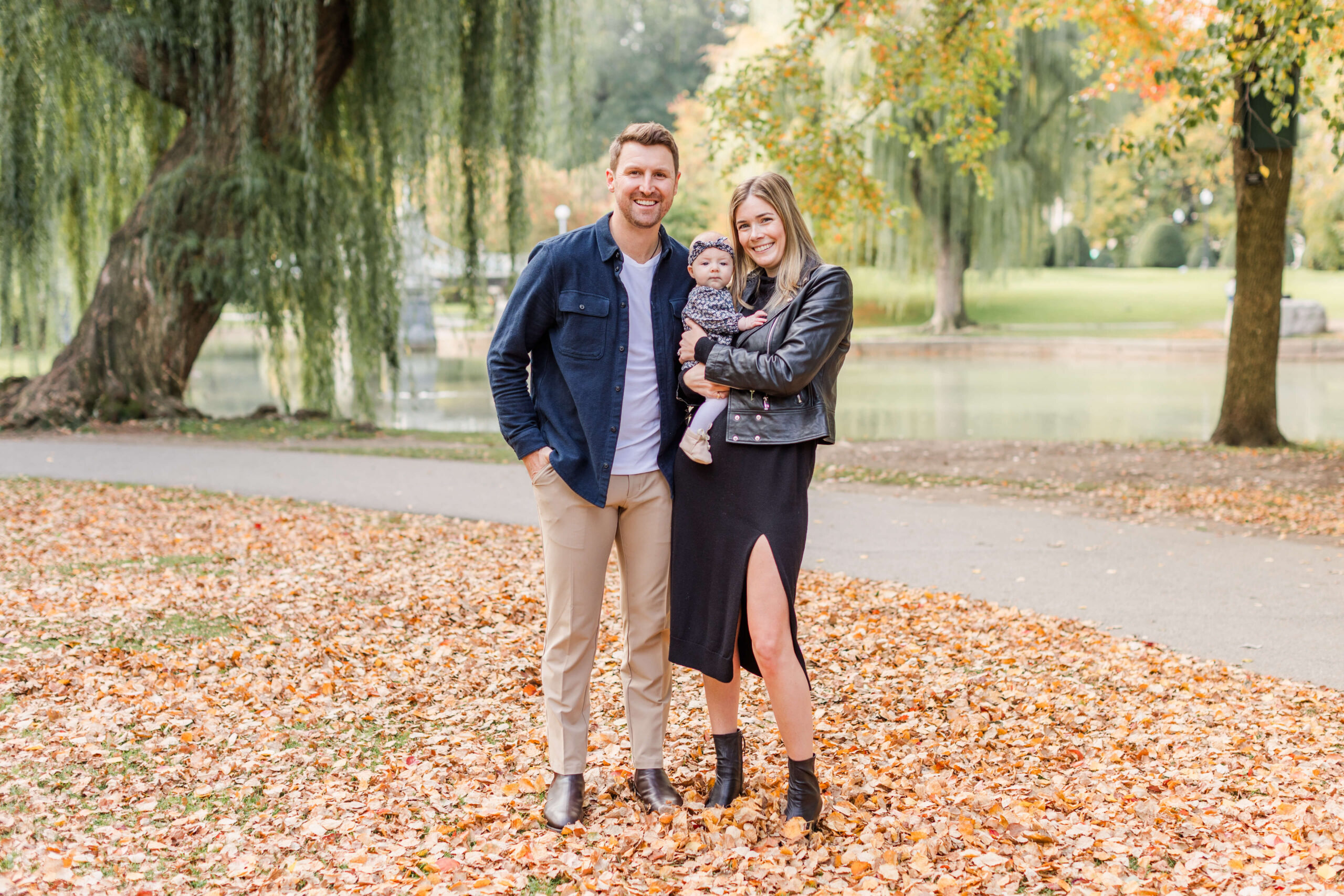 Family of three posing with their baby beside the lagoon during a fall mini session at Boston Public Garden.