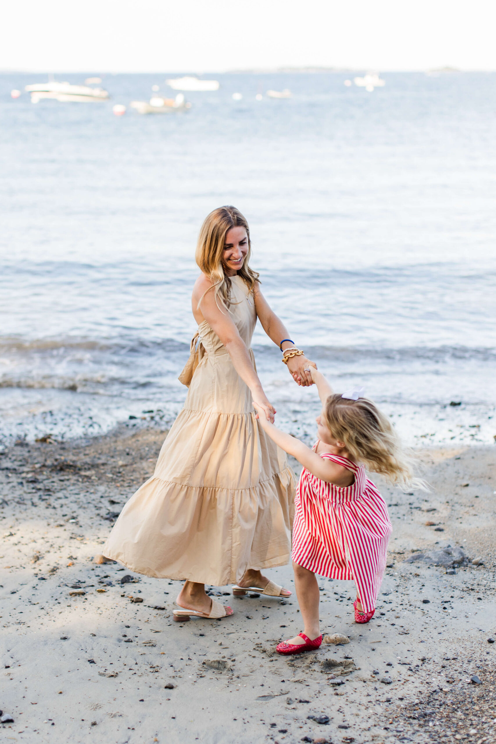 Mother holding hands with her young daughter as they twirl together along the shoreline.