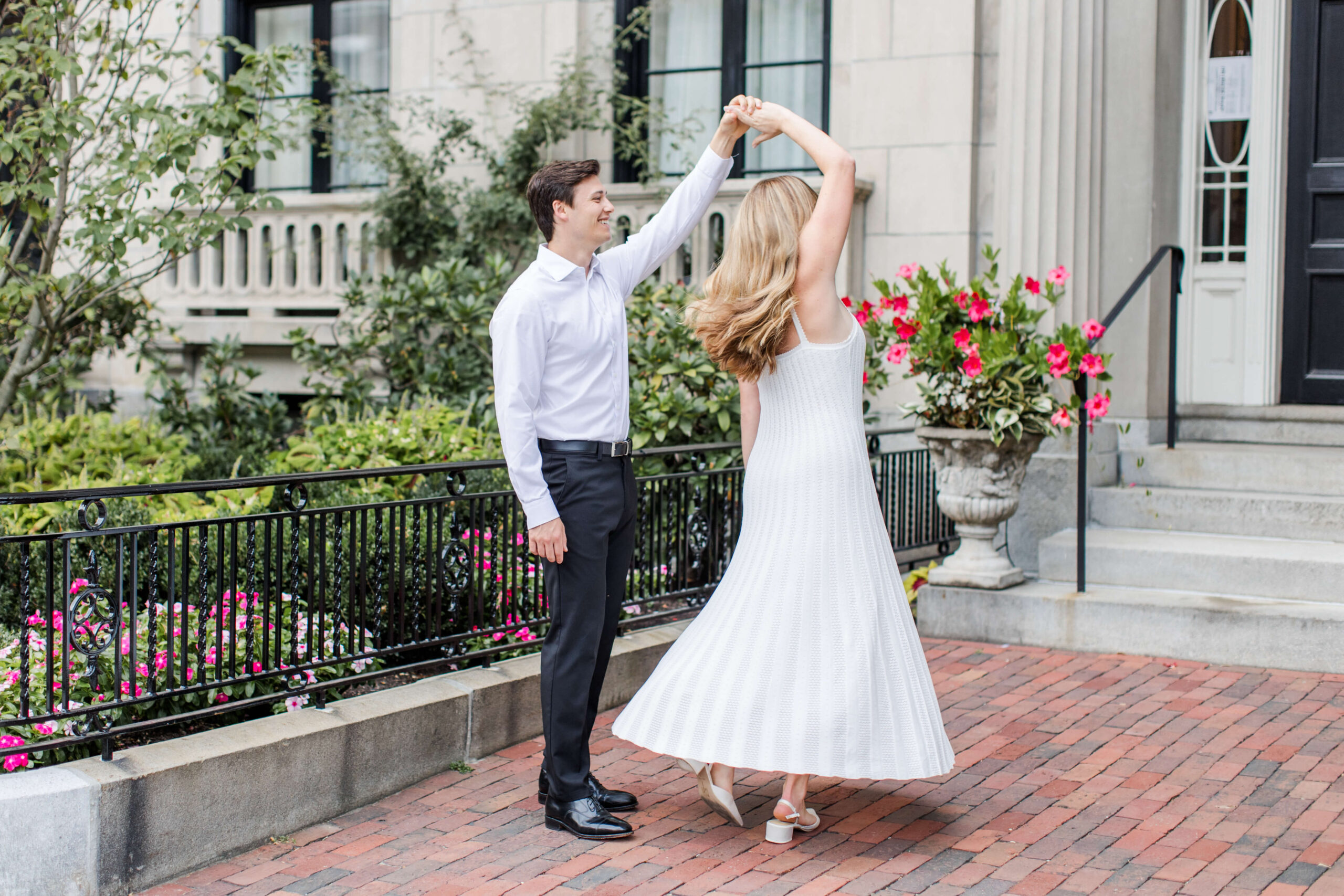 Couple dancing together on a brick sidewalk outside a historic Boston home during an engagement photo shoot.