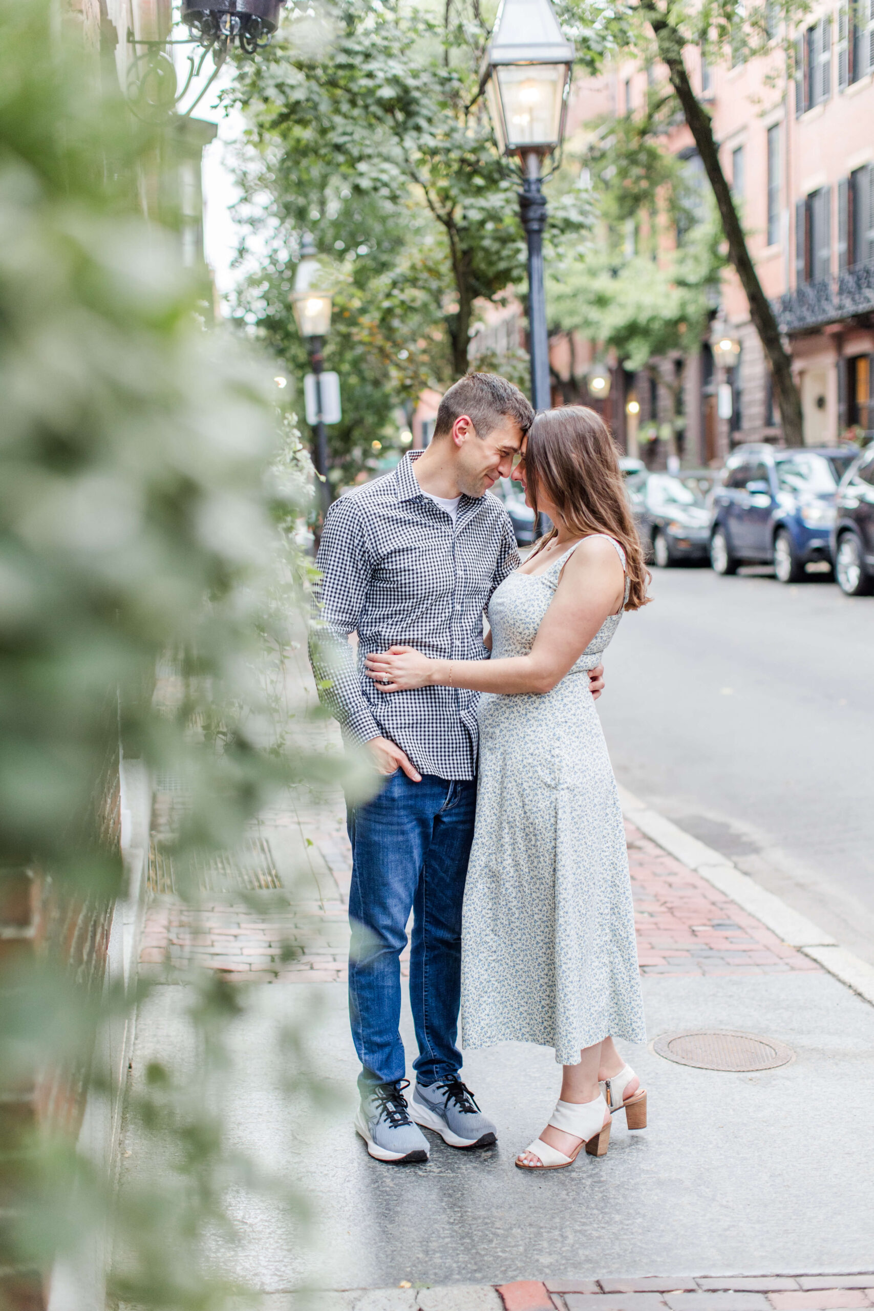 Couple standing close together on a brick sidewalk lined with historic brownstones during a Boston photo shoot.
