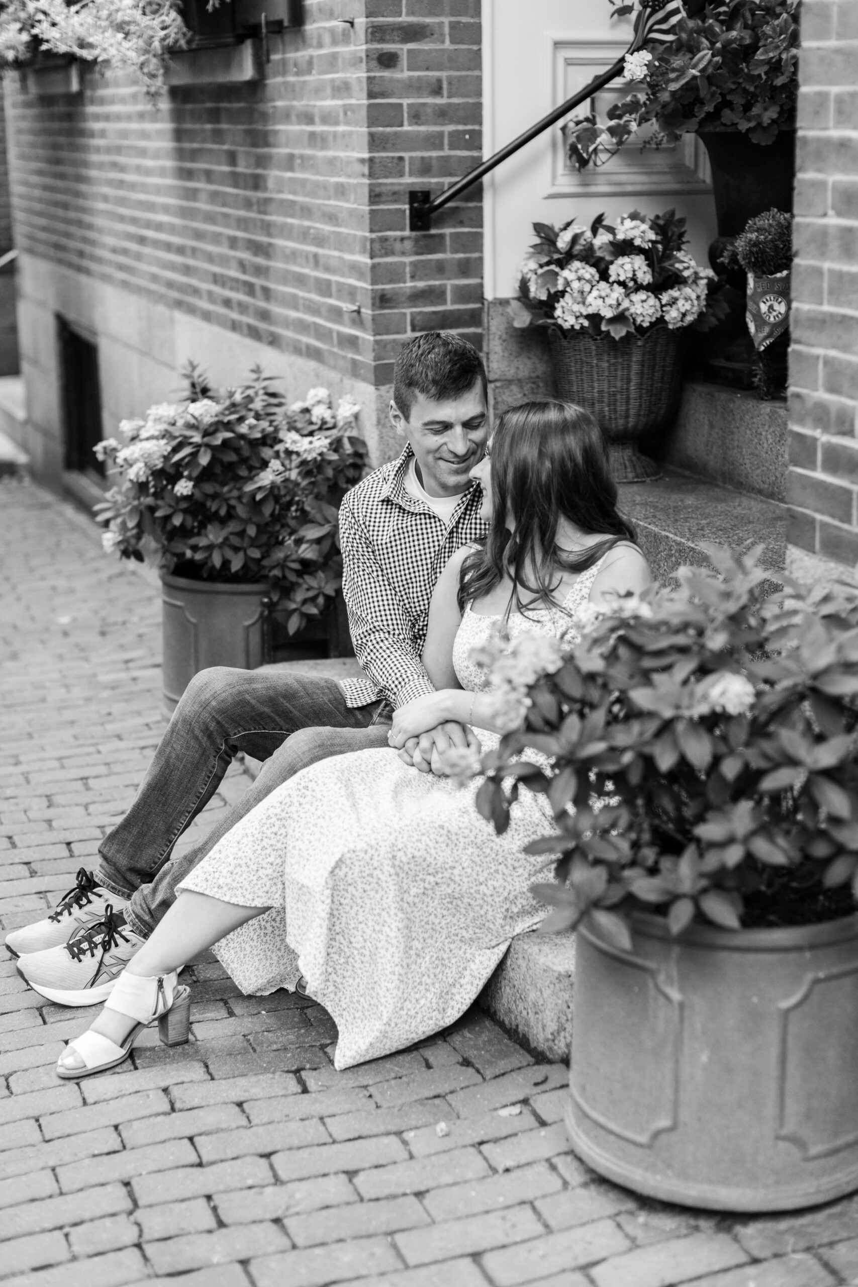 Couple sitting closely together on a brick stoop in a black-and-white portrait during a Boston photo shoot.