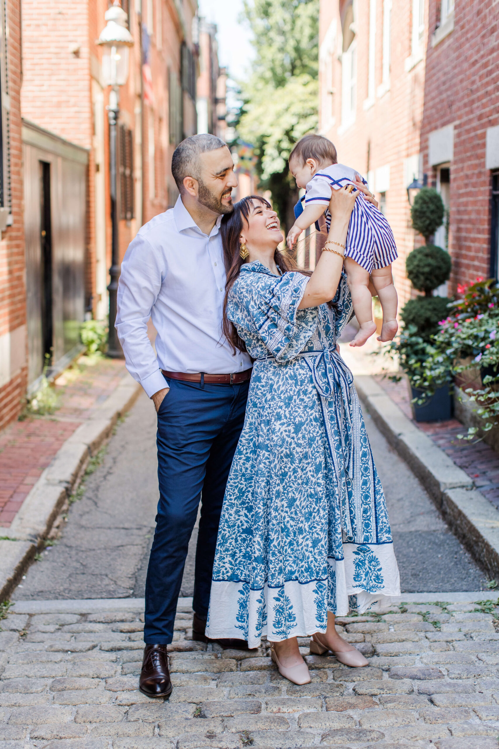 Parents playing with their baby on a cobblestone street lined with historic brick homes in Boston.
