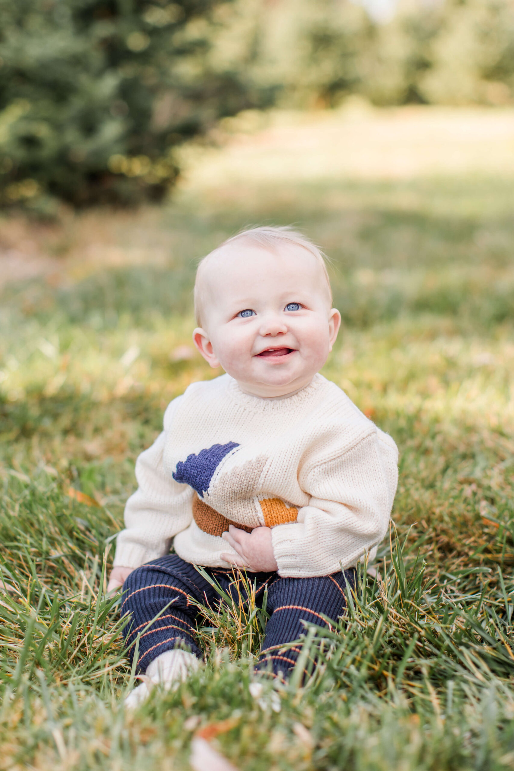 Smiling baby sitting in the grass during a Christmas tree farm mini session.